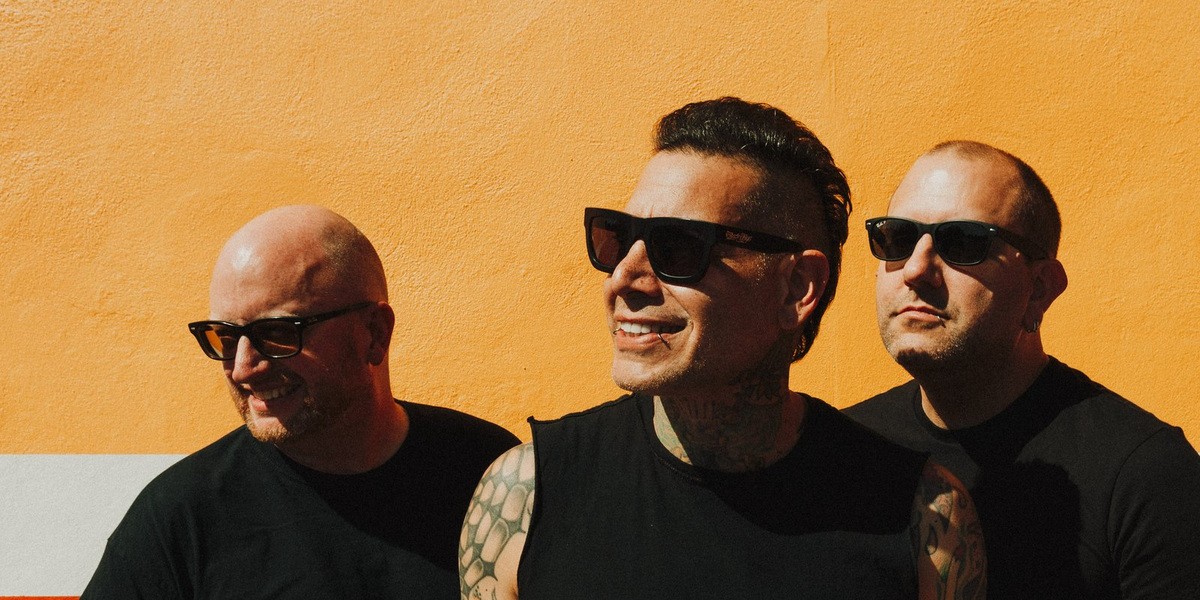 The three members of MxPx standing against an orange wall
