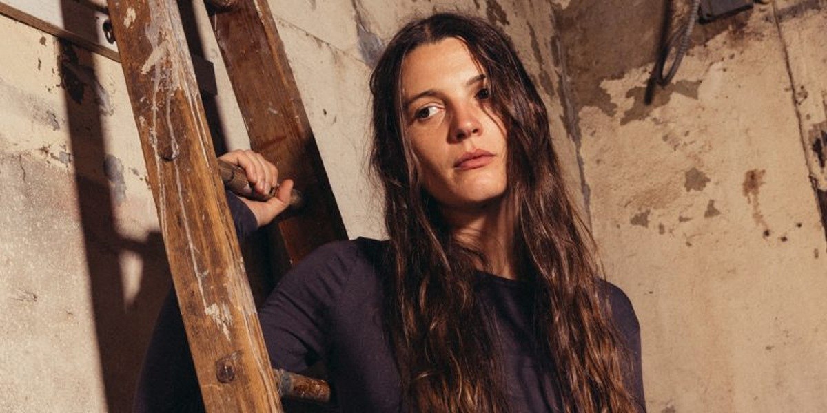 Sophia Stel standing beside a wooden ladder in a promotional portrait